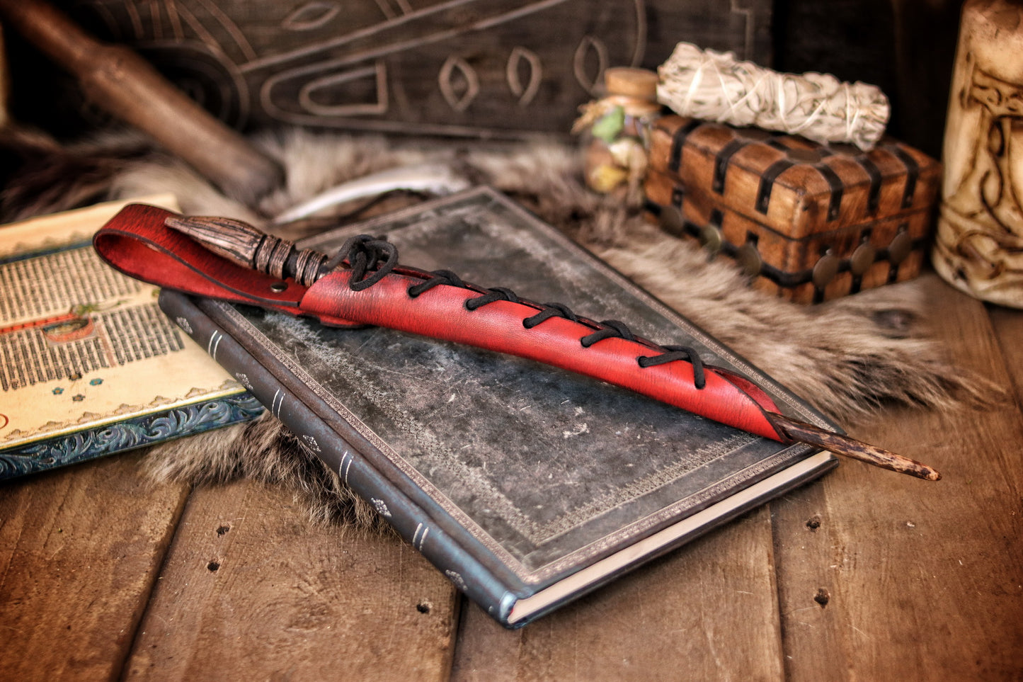 A close-up image of a brown wand holster with a leather strap and lace detail, displayed on an open book with a decorative background. Magic Wand Leather Holster Laced & Aged, perfect sheath for wizzards to hang from your belt, witch wand belt seath cosplay LARP
