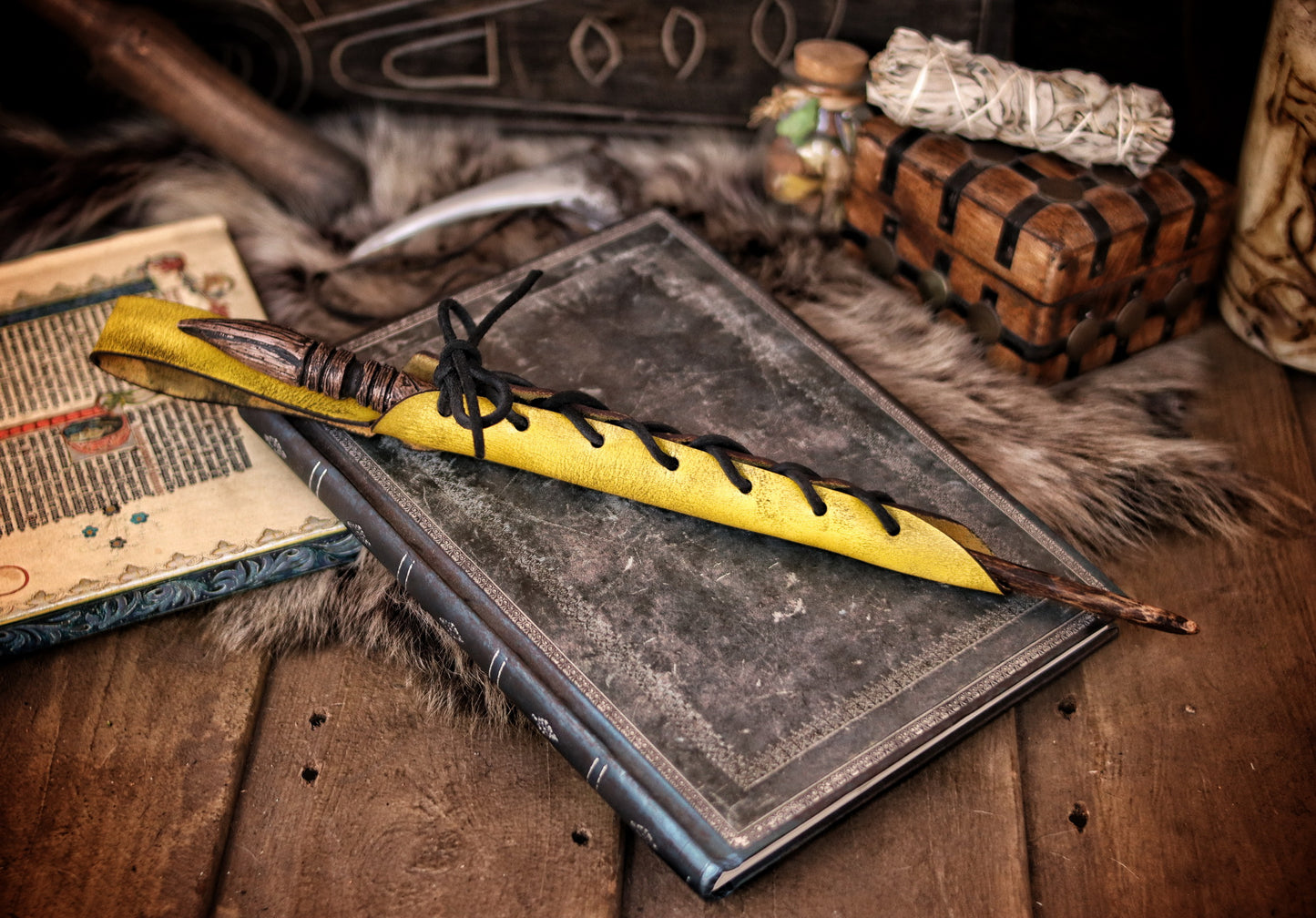 A close-up image of a brown wand holster with a leather strap and lace detail, displayed on an open book with a decorative background. Magic Wand Leather Holster Laced & Aged, perfect sheath for wizzards to hang from your belt, witch wand belt seath cosplay LARP