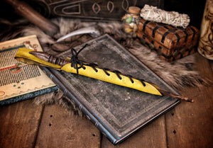 A close-up image of a brown wand holster with a leather strap and lace detail, displayed on an open book with a decorative background. Magic Wand Leather Holster Laced & Aged, perfect sheath for wizzards to hang from your belt, witch wand belt seath cosplay LARP