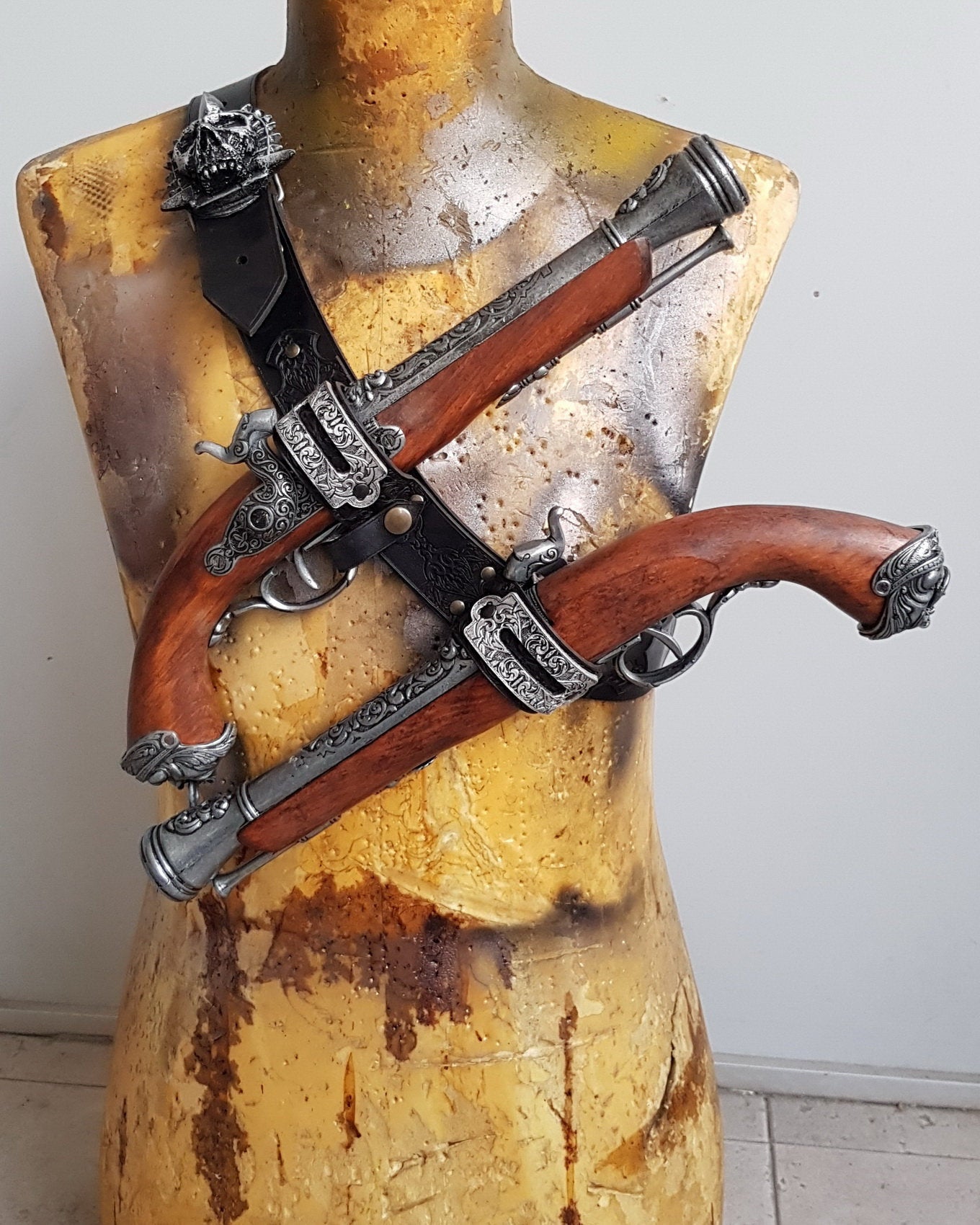 Mannequin torso wearing a handcrafted leather baldric inspired by Edward Kenway from Assassins Creed Black Flag. Two ornate flintlock pistols are crossed over the chest, held by engraved silver holsters. This pirate leather holster is ideal for LARP, pirate cosplay, or Caribbean rogue costumes. The rugged torso and wooden base enhance the adventurous, battle-worn look.