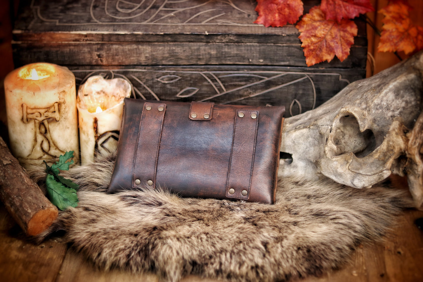 Back view of handmade medieval leather pouch showing dual belt loops. Perfect fantasy accessory for LARP belt attachment. Dark brown vegetable-tanned leather over fur, candles and skull nearby. Shows practical design for wearing on costume. Ideal alt text for accessibility and SEO: LARP leather belt pouch with back loops for secure fit.