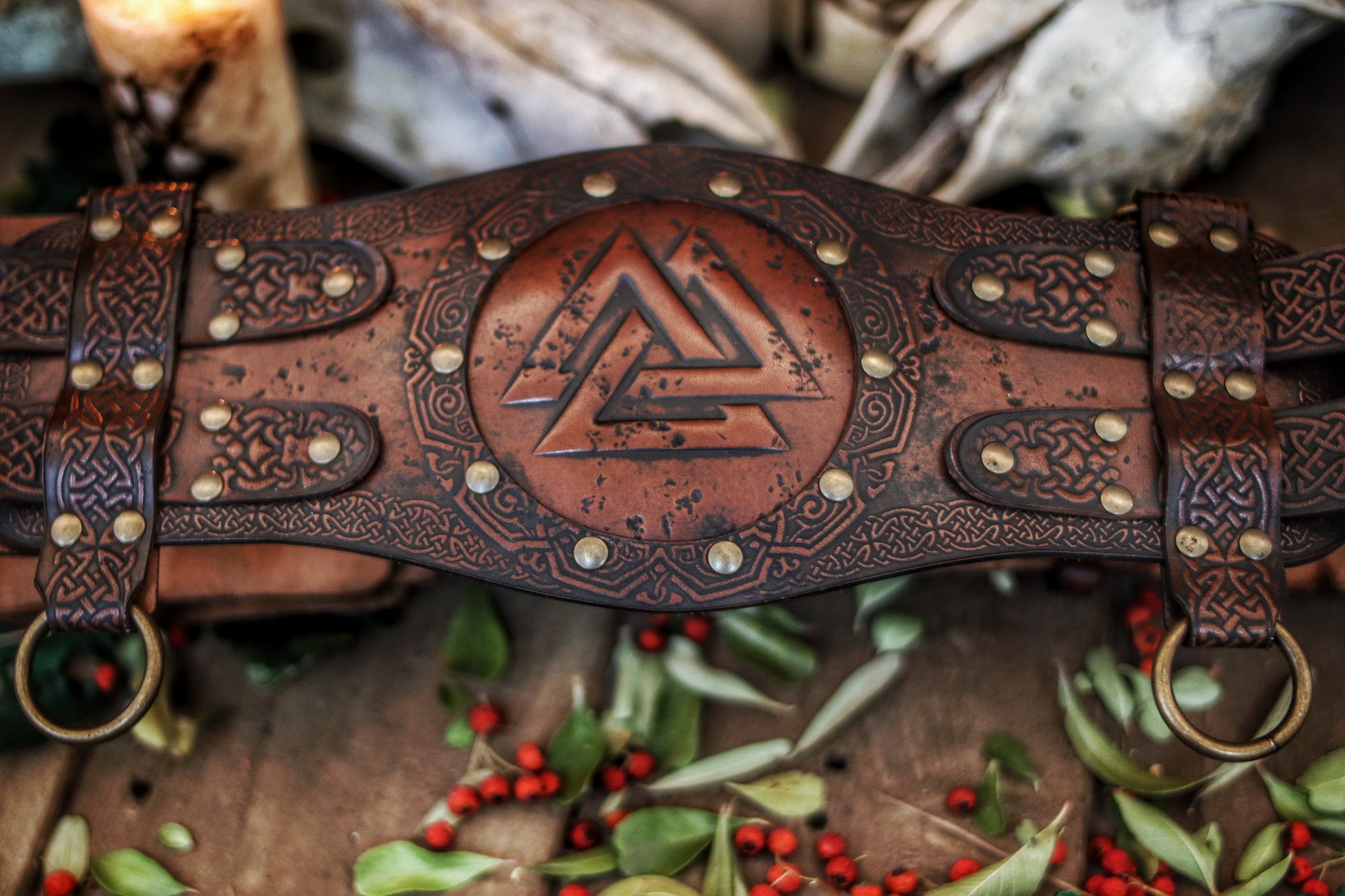 Valknut viking belt placed between burning candles and animal skulls on a wooden floor with leaves and berries. Emphasizes the mystical LARP aesthetic. Long tails: viking leather armor belt, celtic fantasy belt, renfaire costume wide, barbarian cosplay outfit, fantasy medieval warrior accessory. Perfect for immersive roleplay photoshoots.