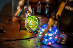 Close-up of two glowing Magic Light Potion Bottles with colorful LED lights inside, wrapped in steampunk-style leather straps. Perfect for LARP, cosplay, Burning Man, or mad scientist costumes. 250ml PET plastic bottles, belt loop included, battery operated with safe LR44 alkaline batteries for aerial transport.