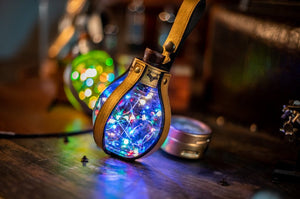 Steampunk glowing potion bottle with multi-colored LED lights, perfect accessory for LARP, Burning Man, or mad scientist cosplay. Plastic 250ml bottle wrapped in aged leather straps, includes belt loop and safety tab for battery conservation during storage or transport.