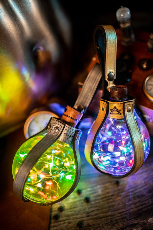 Colorful Magic Light Potion Orbs glowing with tiny LED lights inside PET plastic bottles, secured by steampunk-style leather holders. Great for LARP, cosplay, Burning Man, and fantasy costumes. Battery operated and aerial transport safe, 250ml capacity.