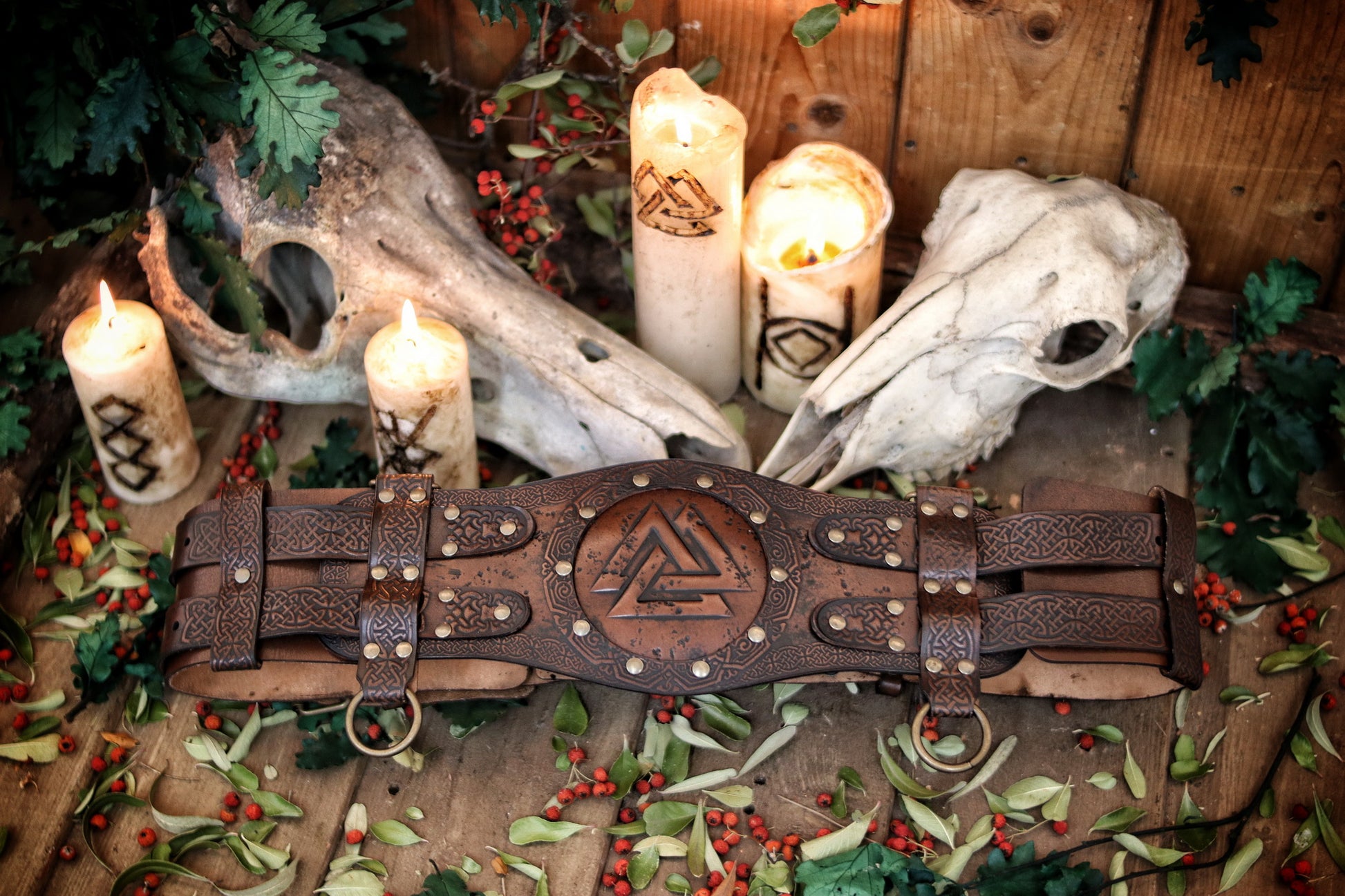 Valknut viking belt placed between burning candles and animal skulls on a wooden floor with leaves and berries. Emphasizes the mystical LARP aesthetic. Long tails: viking leather armor belt, celtic fantasy belt, renfaire costume wide, barbarian cosplay outfit, fantasy medieval warrior accessory. Perfect for immersive roleplay photoshoots.