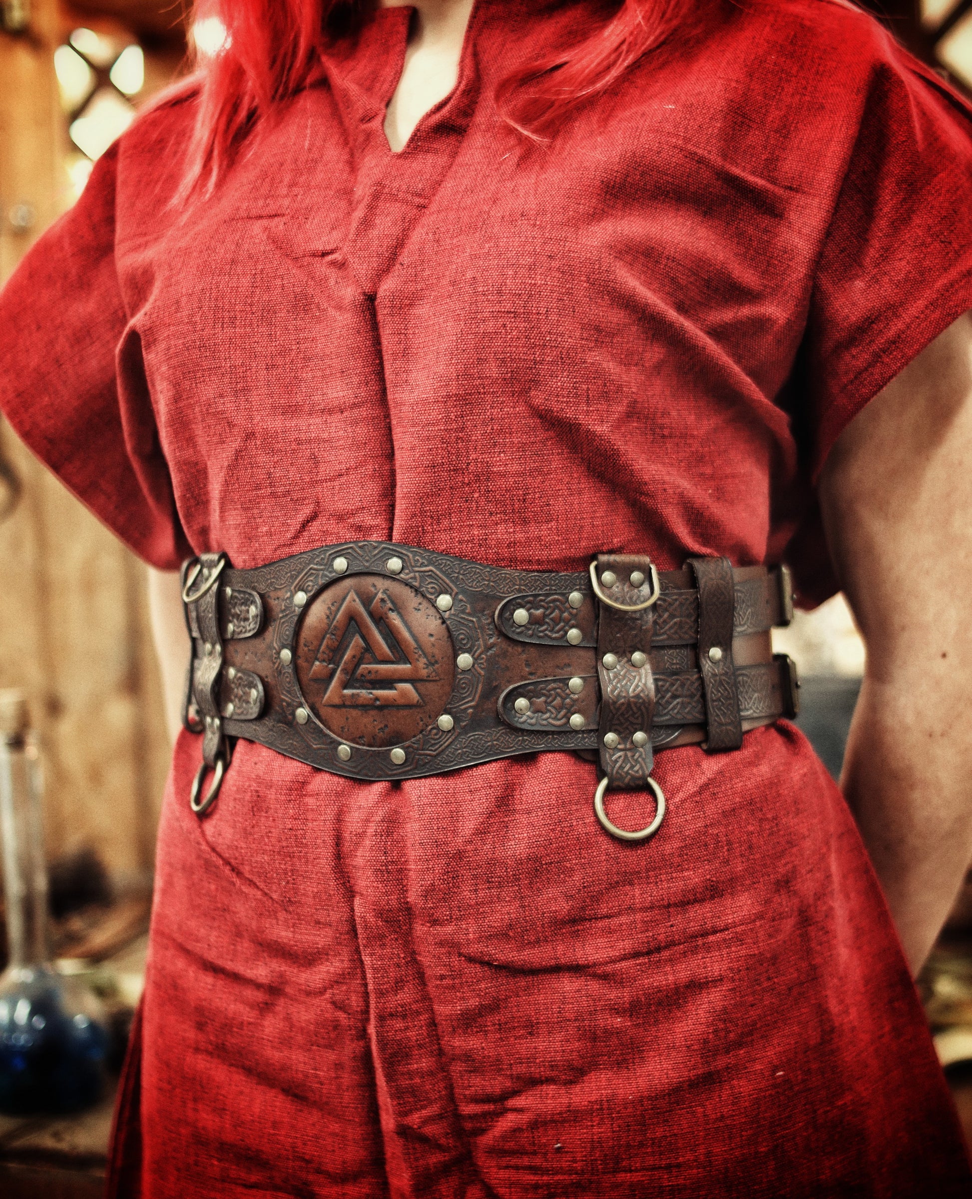 Brown viking leather armor belt on female model in red dress with fur shoulder cape. The belt shows Norse knotwork and a Valknut center, perfect for a celtic fantasy belt or renfaire costume wide. Ideal for LARP warriors or fantasy cosplay. The wide belt enhances the silhouette and secures accessories. Handmade and visually textured.