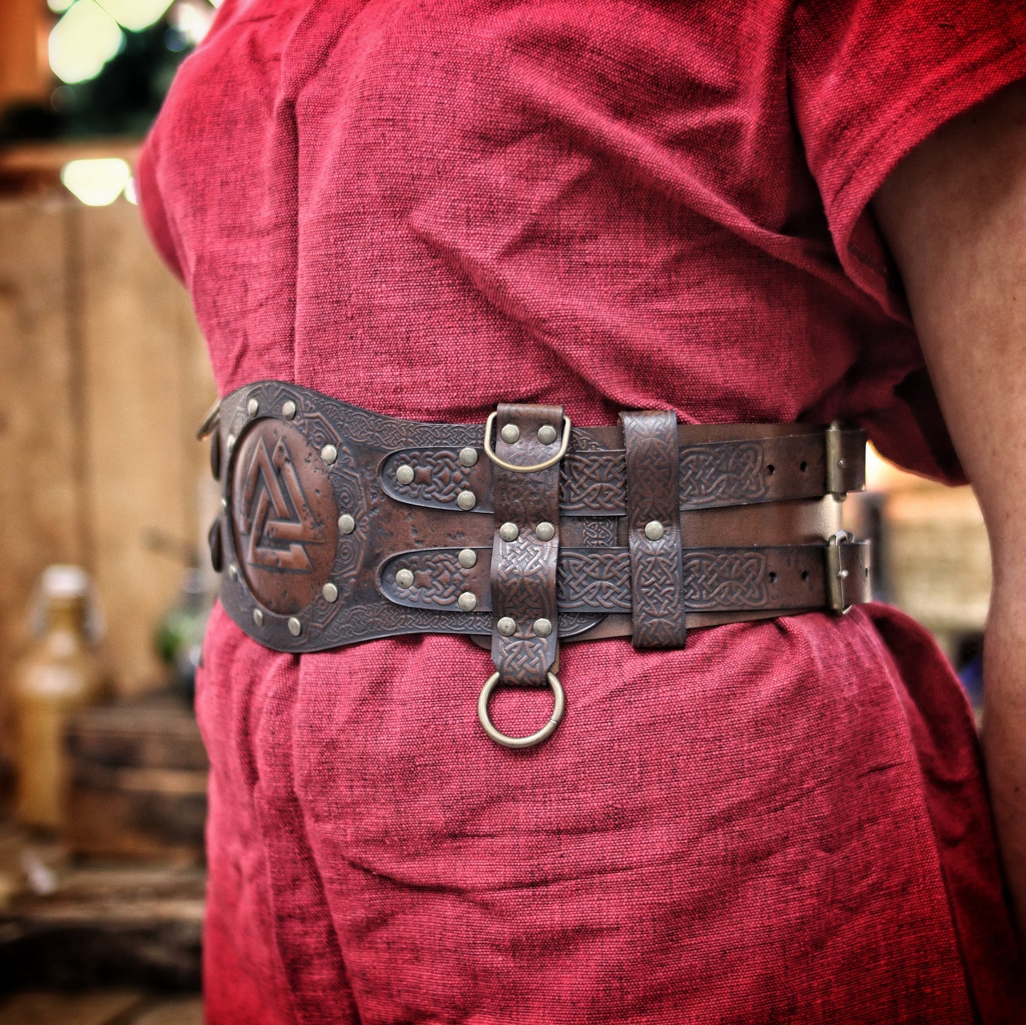 Brown viking leather armor belt on female model in red dress with fur shoulder cape. The belt shows Norse knotwork and a Valknut center, perfect for a celtic fantasy belt or renfaire costume wide. Ideal for LARP warriors or fantasy cosplay. The wide belt enhances the silhouette and secures accessories. Handmade and visually textured.