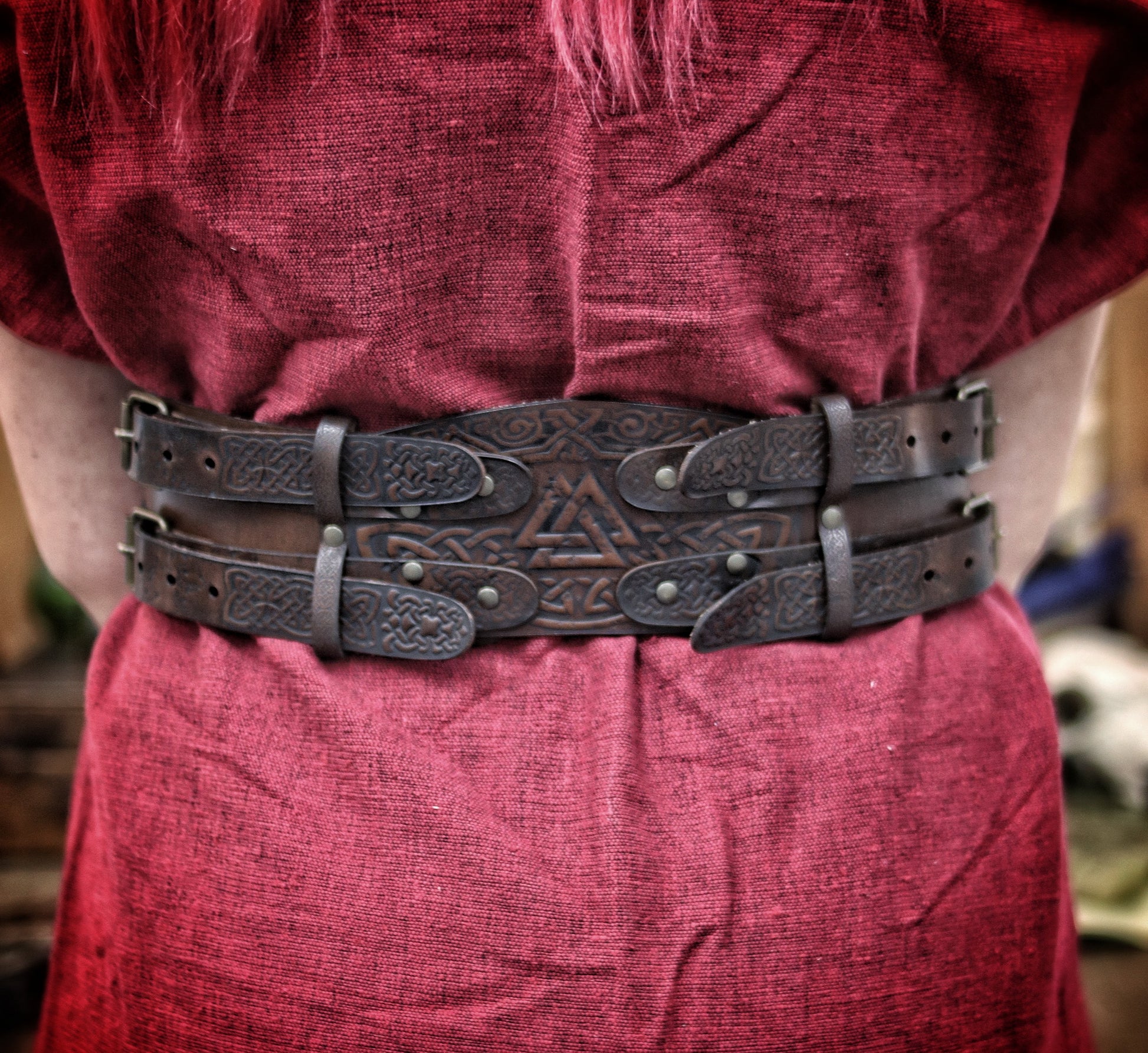 Back view of the leather celtic fantasy belt on a woman in red dress and fur mantle. The viking leather armor belt curves at the waist with detailed knotwork and sturdy brass buckles. Great for medieval warrior armor, barbarian cosplay outfit, or renfaire costume wide. SEO optimized for larp gear and fantasy accessory needs.