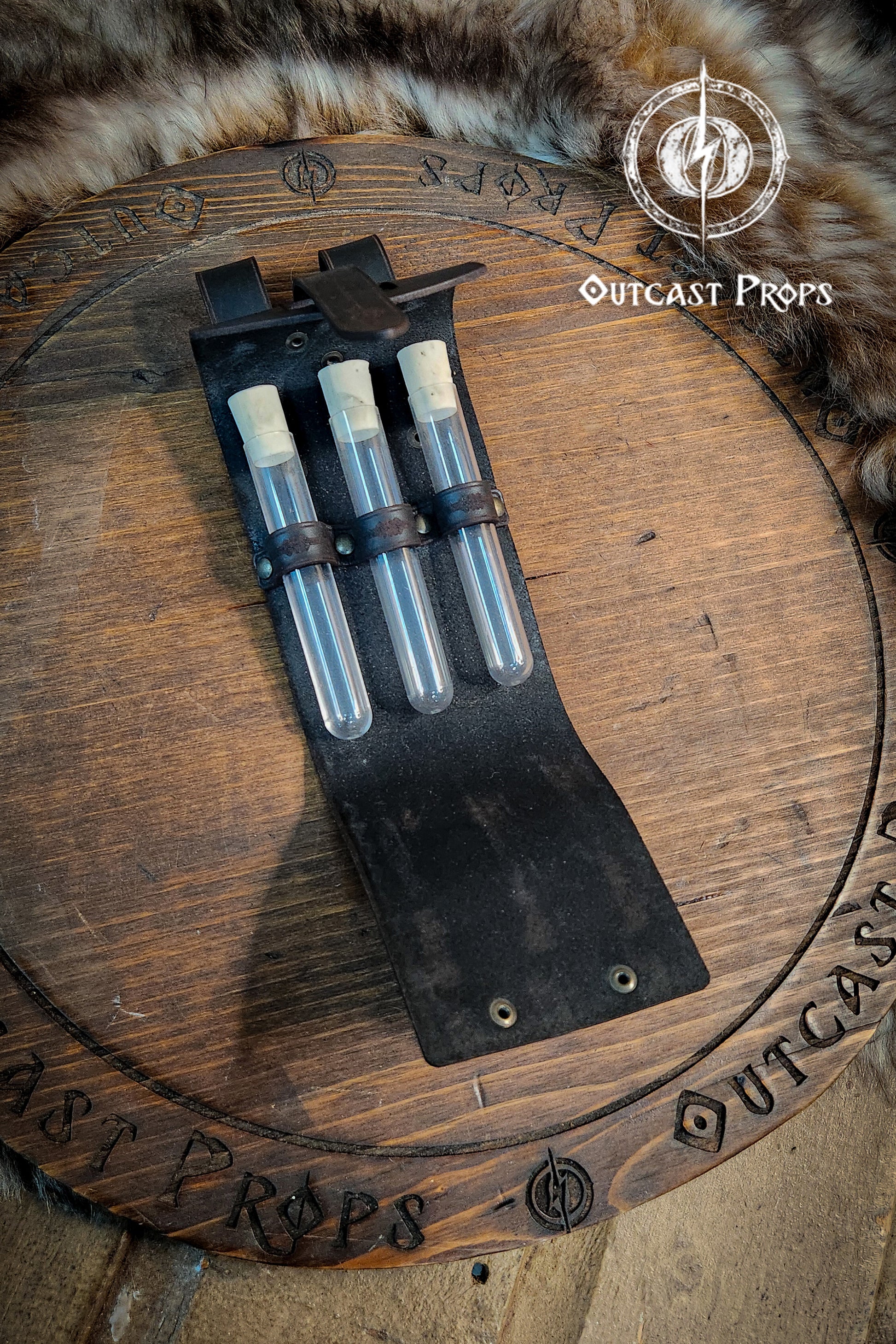 Set of three vials in a leather case on a wooden surface with 'Outcast Props' branding. Leather Vial Case for 3 plastic vials. Adventurers, steampunk, alchemist, healers, cosplay or just to keep spices