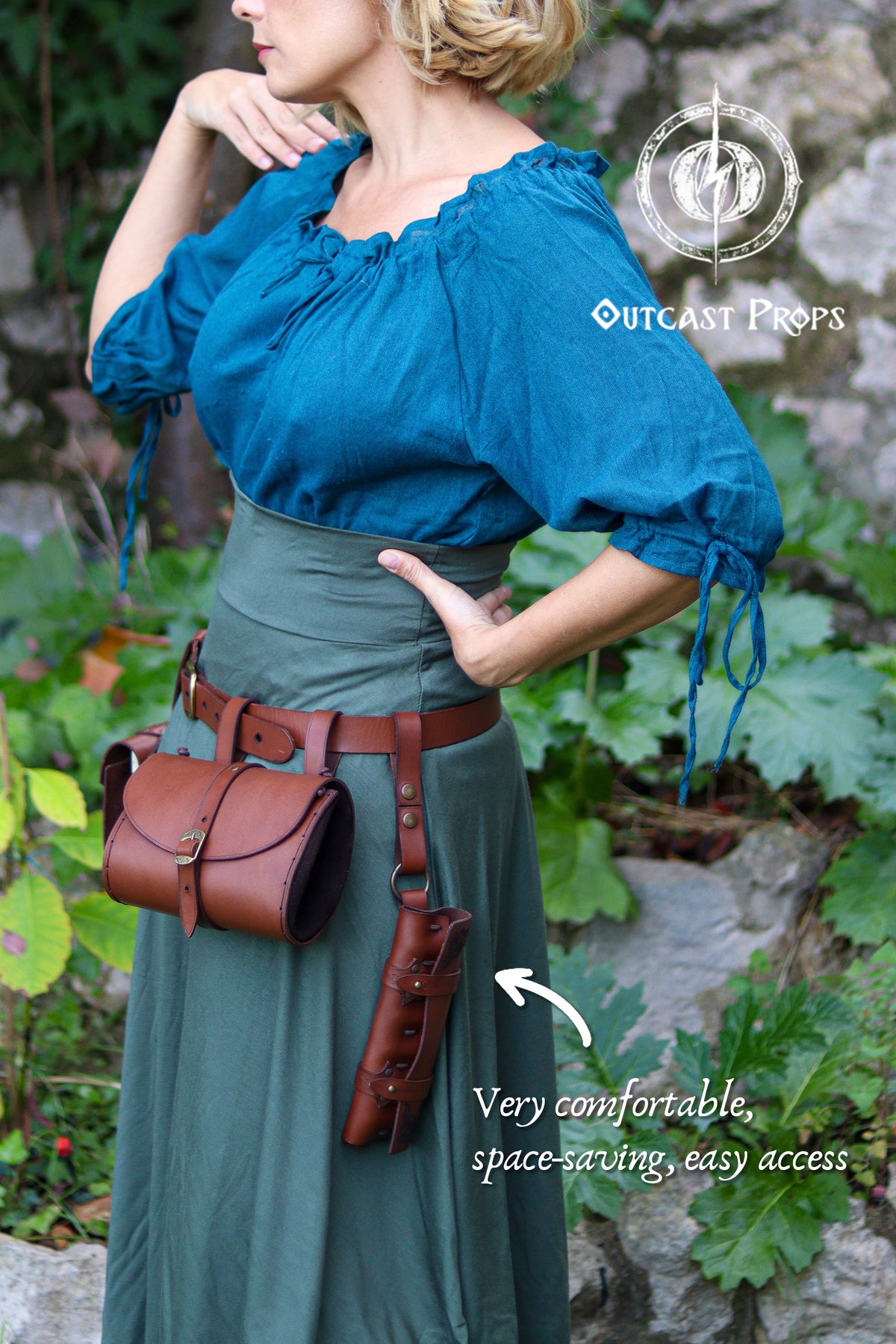 Side view of the potion holster worn at the hip, hanging vertically from a brown leather belt over a green skirt and teal blouse. The small cylindrical case holds six vials tightly and is paired with a matching pouch, forming a full alchemist belt kit. The wearer poses outdoors near stone and foliage, evoking a fantasy setting. Designed for LARP alchemist characters, wizards, nobles or rogues, the compact holster keeps potions, spices or herbs accessible while saving space on steampunk or larp belts.