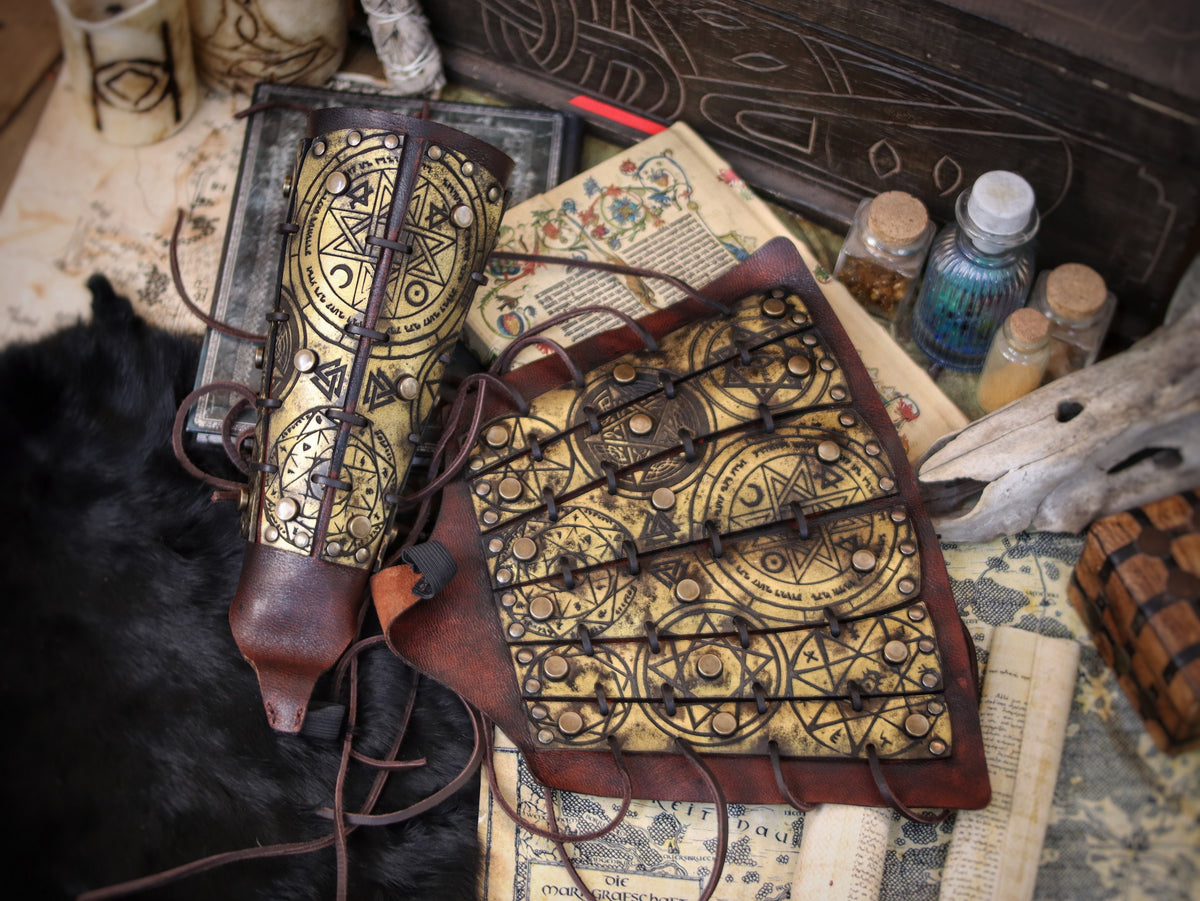 Golden fantasy bracers with matching armguard, engraved with magical runes and ritual symbols, shown in an arcane tabletop scene with scrolls and potions. Perfect for LARP witch armor, warlock costume or alchemist outfit. Handmade with aged leather and adjustable laces, these vambraces are a high-quality accessory for medieval, fantasy or occult cosplay enthusiasts.