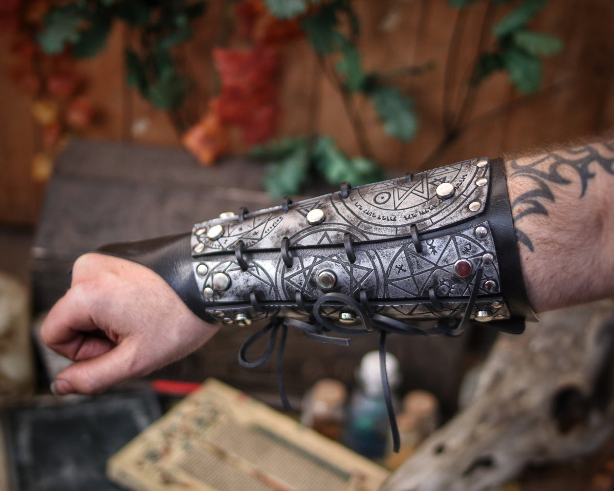 Silver leather bracer for LARP and fantasy cosplay, engraved with alchemical symbols and mystical geometry. Decorated with metal studs and polished beads for a gothic warlock or dark wizard look. Handmade from vegetable-tanned Spanish leather, adjustable and resistant. Perfect for witches, ritualists, or demon hunters in immersive fantasy roleplay.