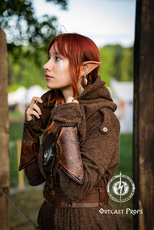 Person in fantasy costume with brown outfit and elven ears outdoors. Viking Leather Bracers with Norse Knot Engraving for LARP Cosplay Medieval Fantasy Roleplay Handmade Armor Custom Gear for Men or Women