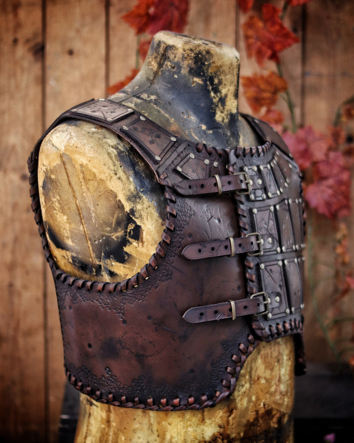 A handmade leather studded armor displayed on a wooden stand with a fur cape, featuring brown leather plates with studs, and a corded edge finish. Barbarian studded leather chest armor with rabbit fur cape attachment shown on mannequin. Perfect for fantasy LARP, Viking reenactment or cosplay, this full-grain leather armor is aged by hand and paired here with fur for an epic look. Adjustable buckle straps and visible stitching add to the rugged charm of this high-impact warrior costume piece.