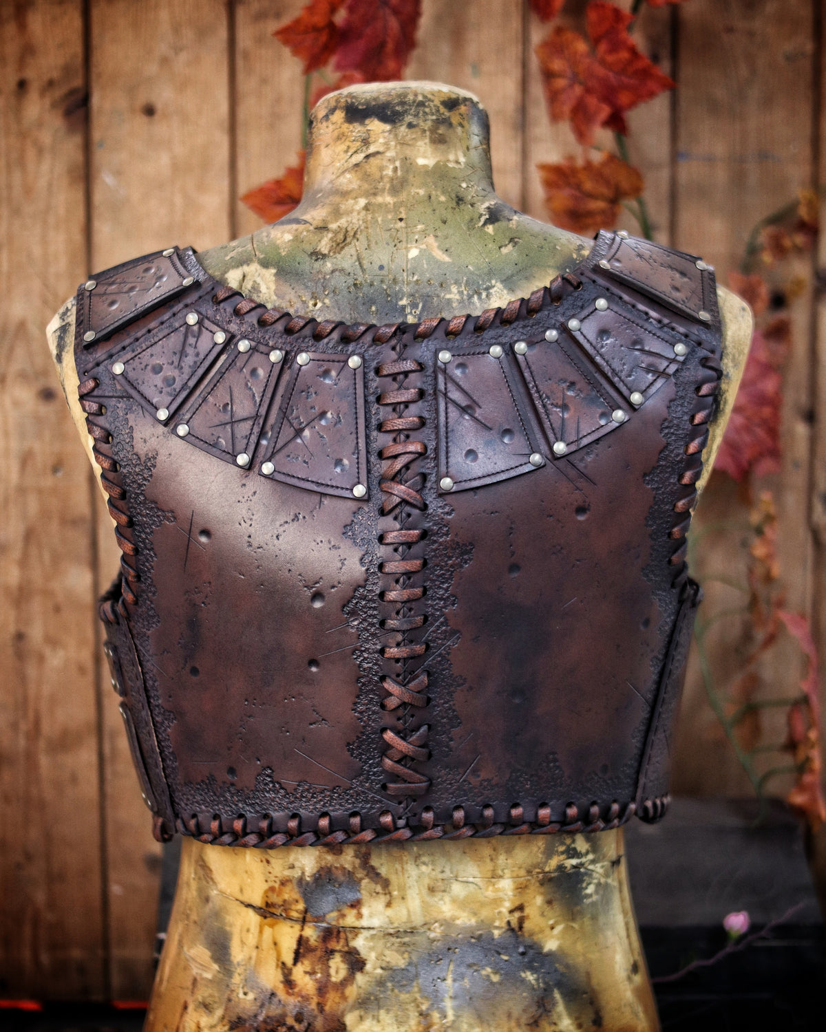 A handmade leather studded armor displayed on a wooden stand with a fur cape, featuring brown leather plates with studs, and a corded edge finish. Barbarian studded leather chest armor with rabbit fur cape attachment shown on mannequin. Perfect for fantasy LARP, Viking reenactment or cosplay, this full-grain leather armor is aged by hand and paired here with fur for an epic look. Adjustable buckle straps and visible stitching add to the rugged charm of this high-impact warrior costume piece.