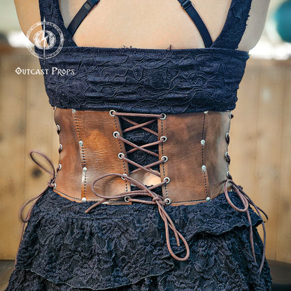Back view of the aged brown witch leather corset featuring symmetrical lacing for adjustable fit. Made from full-grain vegetable-tanned leather with nickel rivets, this underbust corset enhances gothic and steampunk outfits. Ideal for ren faire costumes or fantasy festivals, it combines historical design and artisan detail. Every Outcast Props corset is hand-aged, making each piece unique in tone and texture.