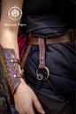 Medieval Persian leather skirt hike in brown, attached to a brown belt and black layered skirt on a fantasy LARP outfit. The accessory displays intricate Alhambra and Persian-inspired patterns and a brass O-ring. This handcrafted leather skirt hiker is designed for ren faire, LARP, fantasy costumes, and cosplay outfits, providing both a practical way to lift skirts or carry accessories and a beautiful decorative detail.