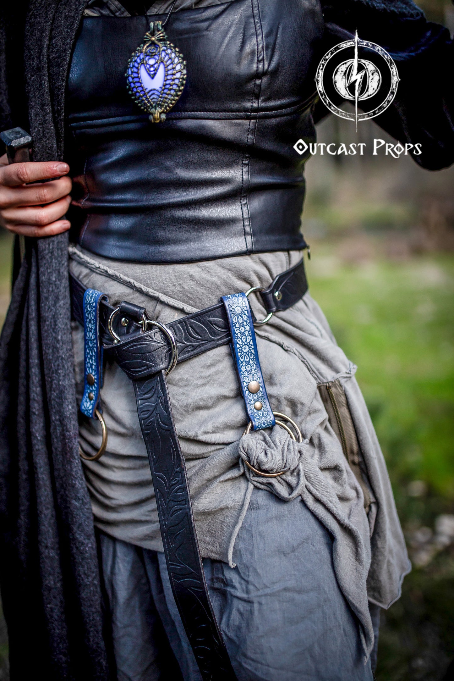 Two blue Persian leather skirt hikes attached to a black fantasy leather belt on a layered grey LARP costume. The skirt hikes, embossed with Arabic Alhambra motifs, feature brass O-rings and snap buttons for functional and decorative use. Ideal for medieval, ren faire, or fantasy cosplay outfits, these handcrafted leather accessories elevate your costume while offering practical versatility for LARP adventurers.