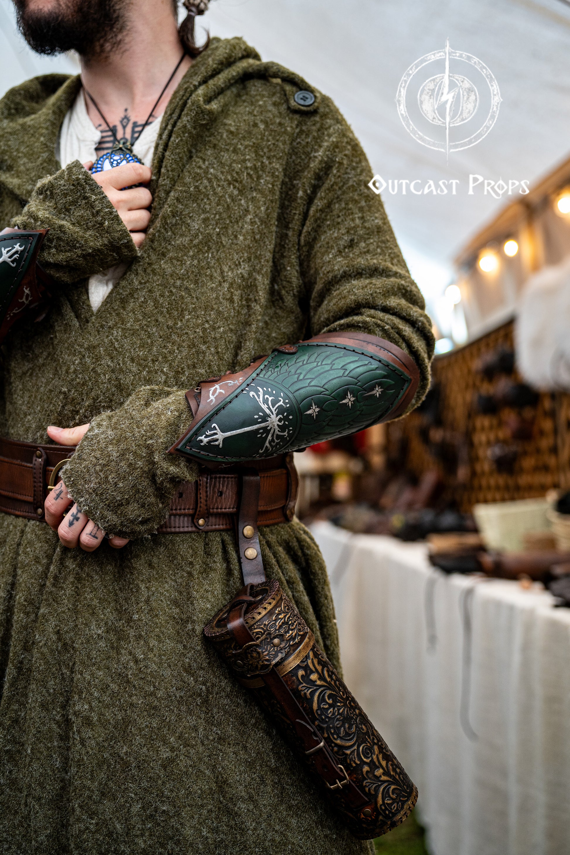 Person in a green robe with leather arm guards and a belt, standing in a market setting.