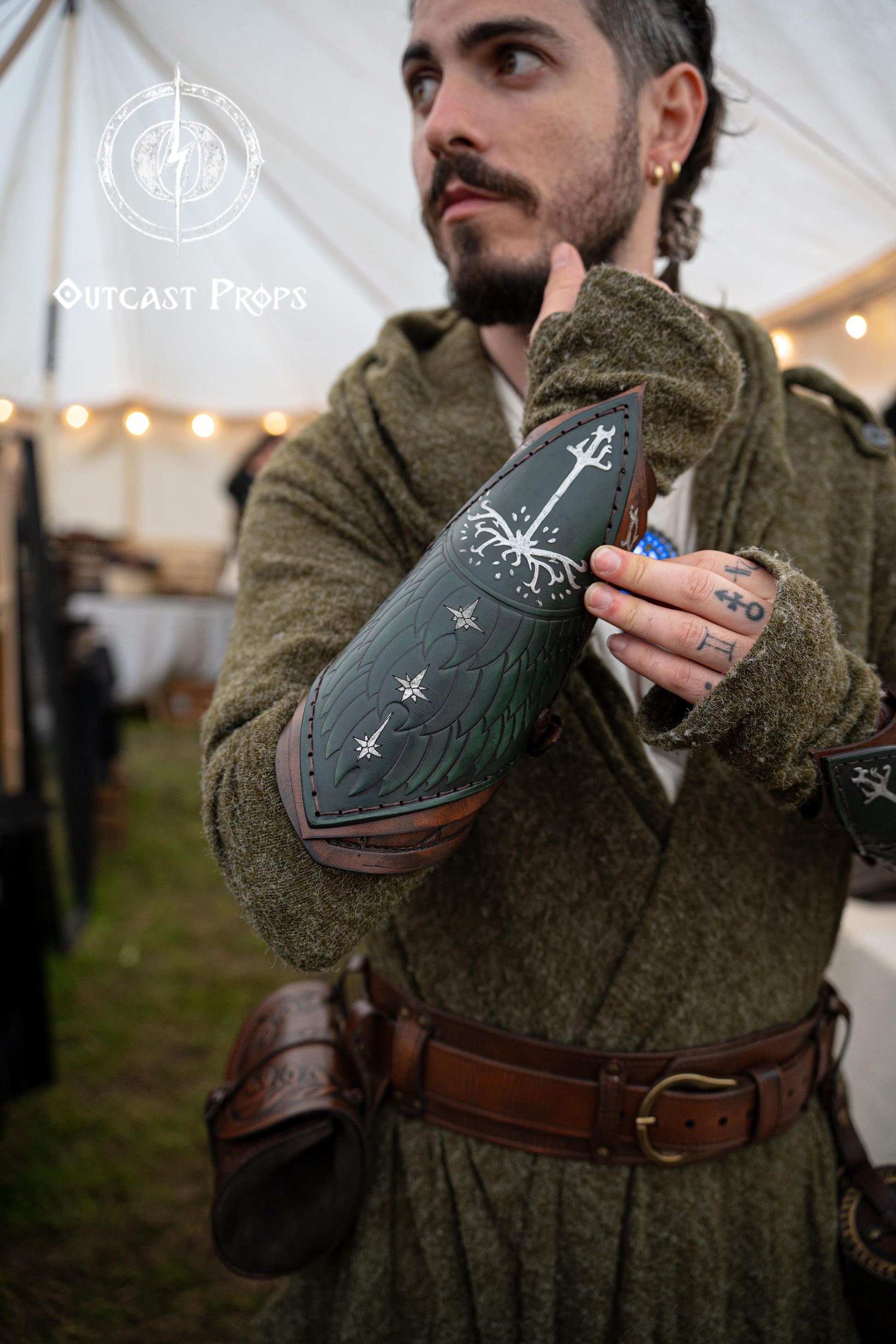 Fantasy LARP costume detail showing green Gondor vambrace engraved with White Tree, worn by an elven ranger. Embossed leather inspired by Aragorn and LOTR aesthetics. Adjustable and handmade, this bracer suits cosplay, Tolkien events, and medieval warriors. Ideal for portraying Gondorian soldiers or Middle-earth scouts. Evokes characters like Boromir, Faramir, and Númenórean descendants.