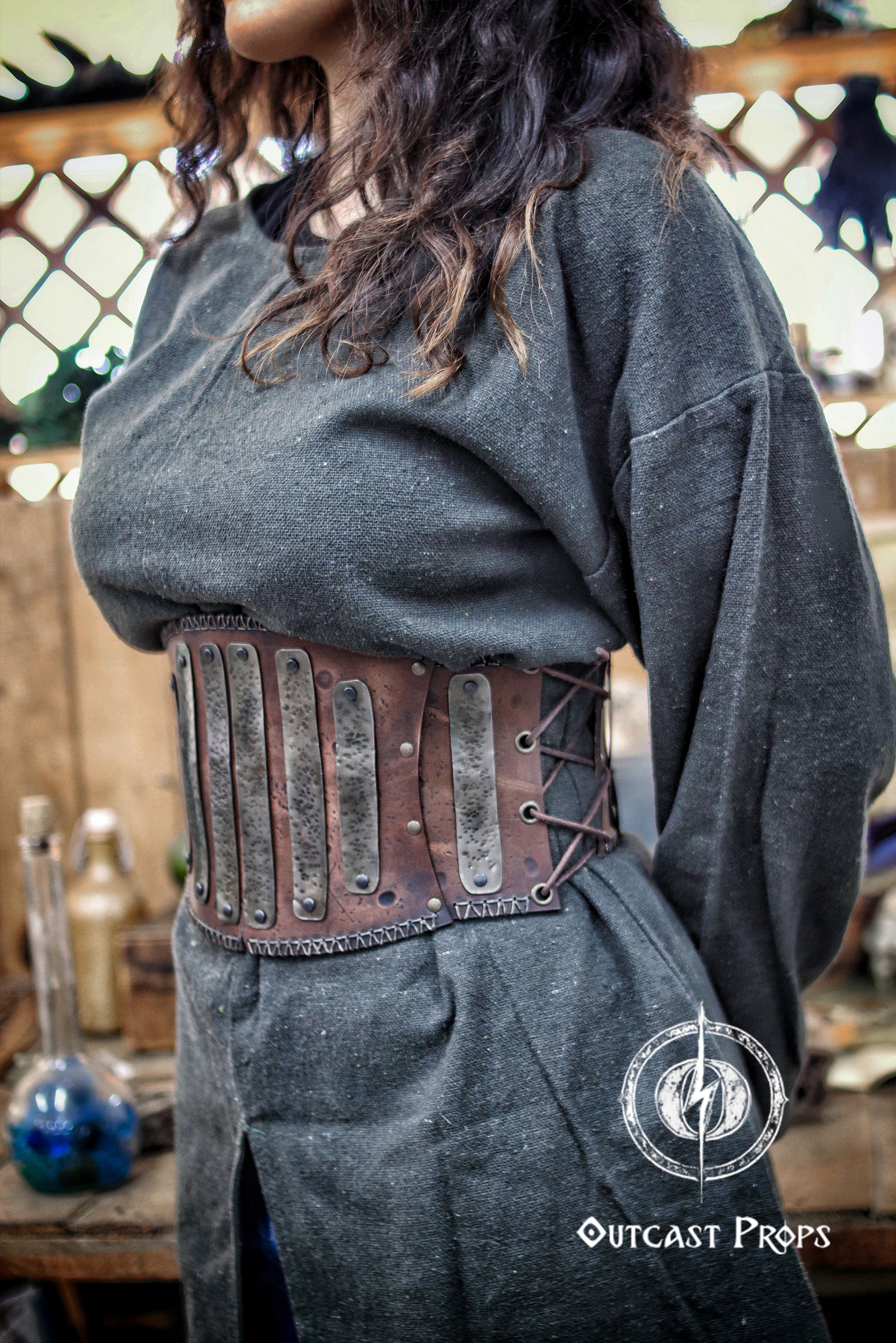 Person wearing a dark gray sweater with a brown leather corset belt, standing in a rustic setting. Barbarian Leather armor woman, larp armor woman viking piece woman post apocalyptic cosplay