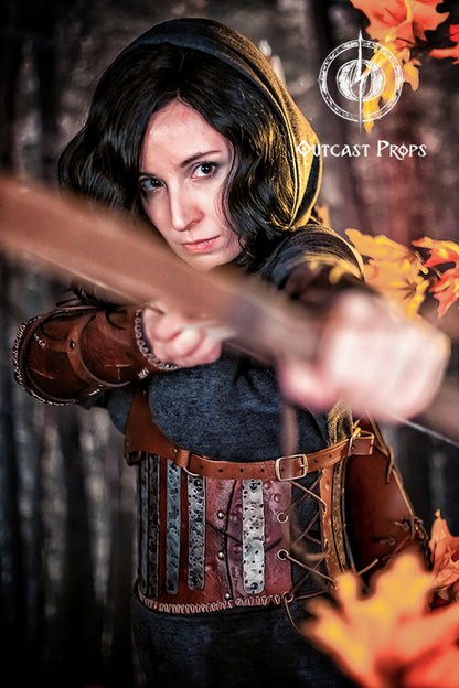 Person in medieval costume holding a bow with 'Outcast Props' branding. Barbarian Leather armor woman, larp armor woman viking piece woman post apocalyptic cosplay