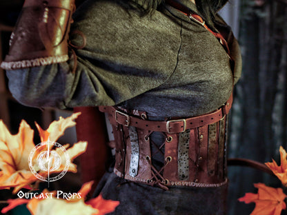 Person wearing a detailed leather belt with metal accents, standing against a dark background with autumn leaves. Barbarian Leather armor woman, larp armor woman viking piece woman post apocalyptic cosplay