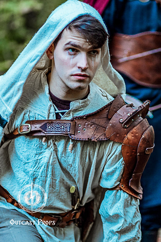 Barbarian Viking Leather Shoulder armor set. Person in medieval or fantasy costume with leather armor and hood, Outcast Props logo visible.