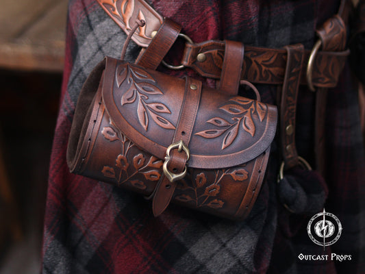 Handcrafted floral leather hip bag pouch shown as part of a renaissance faire costume, made from full grain vegetable-tanned leather with embossed floral motifs and aged brown finish. The leather bag hangs securely from the belt and closes with an easy-to-use buckle, combining historical aesthetics with everyday practicality. Designed for LARP, medieval cosplay and fantasy events, this floral hip bag can hold modern essentials like keys, phone or small notebook while maintaining an authentic medieval look e