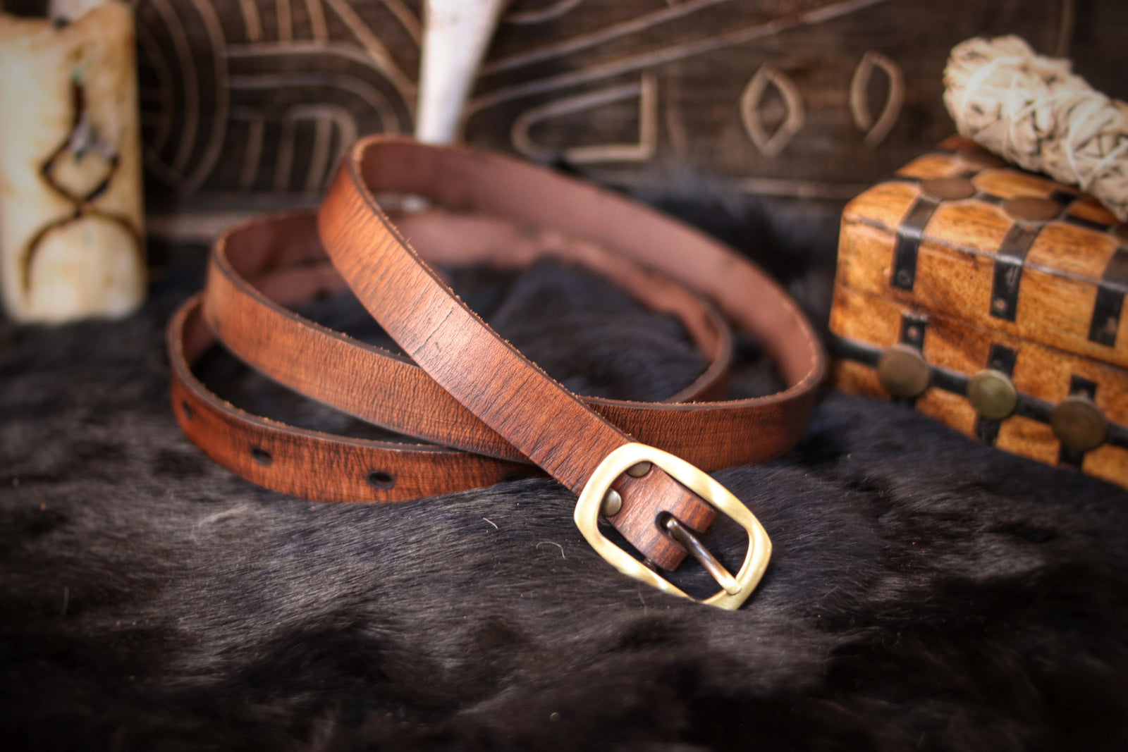 A brown leather belt with a buckle, placed on a furry surface, with props and a storage box in the background. 20 Plain leather belt