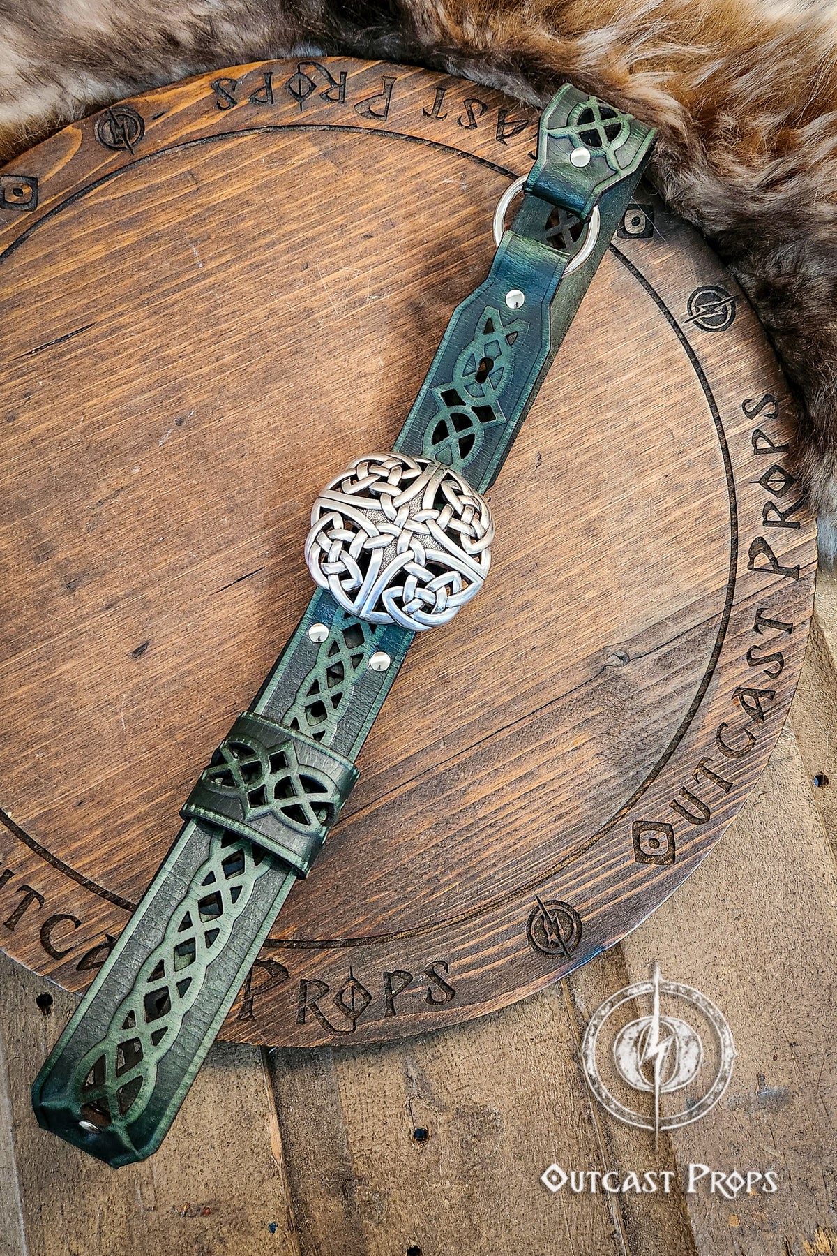 Decorative leather strap with metal ball on a wooden surface, branded 'Outcast Props'.