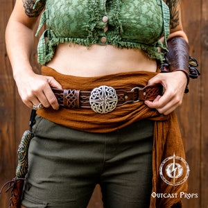 Person wearing a green textured top and brown pants with a decorative belt, standing against a wooden background. Celtic knot leather belt silver buckle larp belt for ren fair fantasy costume celtic belt unisex leather belt for renaissance outfit