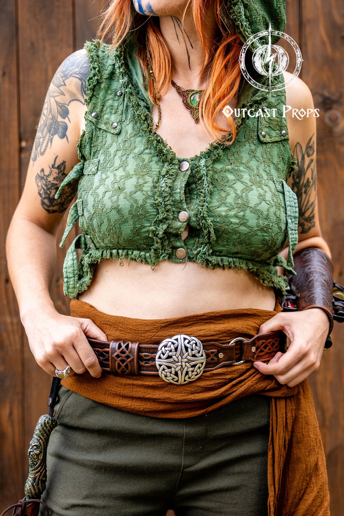 Person wearing a green top and brown pants with tattoos, standing against a wooden background. Celtic knot leather belt silver buckle larp belt for ren fair fantasy costume celtic belt unisex leather belt for renaissance outfit