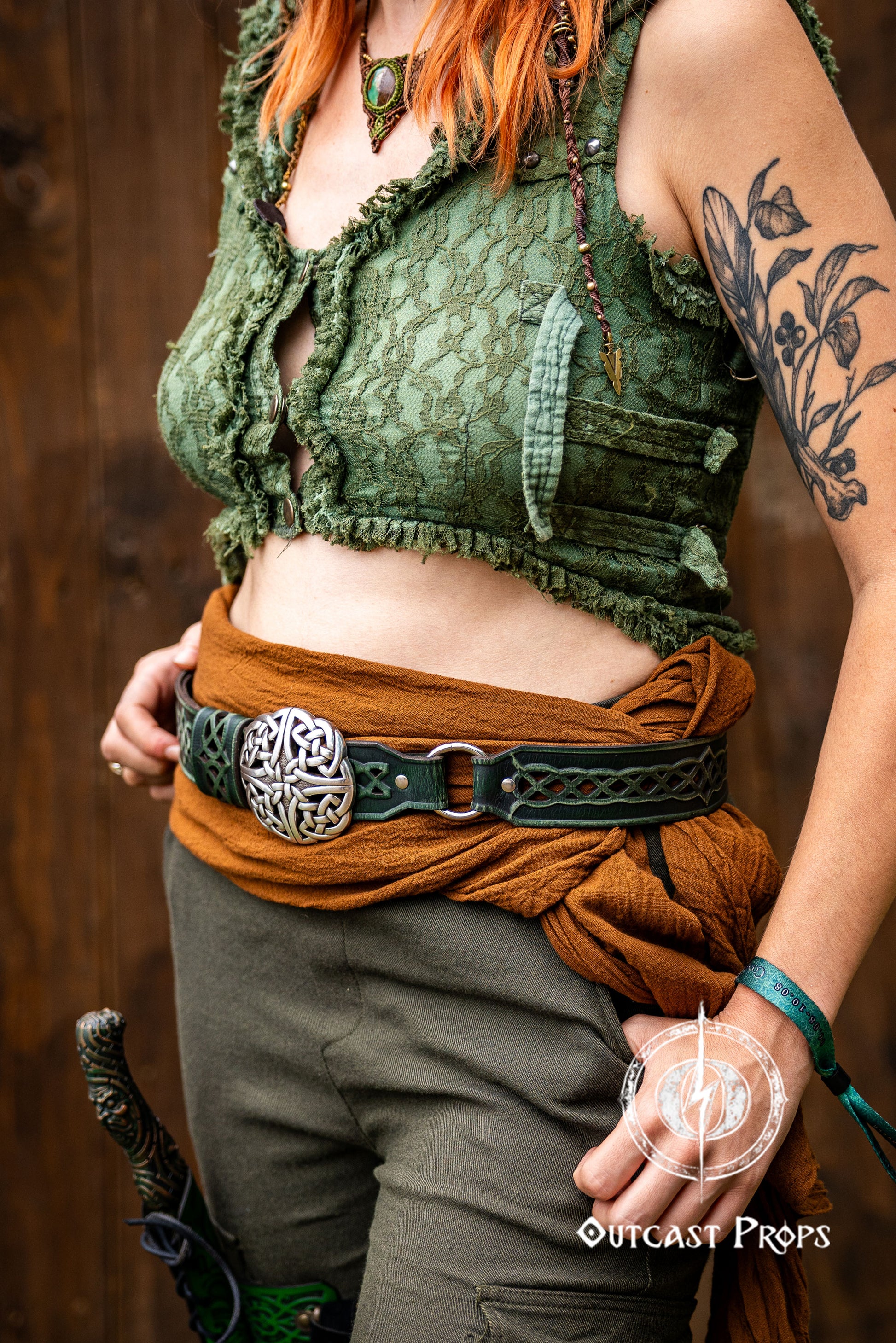 Person wearing a green lace top and brown pants with a belt, standing against a wooden background. Celtic knot leather belt silver buckle larp belt for ren fair fantasy costume celtic belt unisex leather belt for renaissance outfit