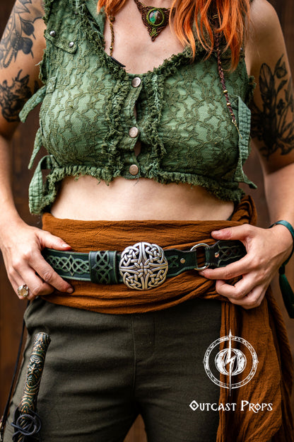 Person wearing a green lace top and brown pants with a belt, holding a sword, against a dark background. Celtic knot leather belt silver buckle larp belt for ren fair fantasy costume celtic belt unisex leather belt for renaissance outfit
