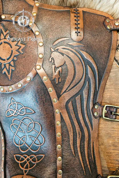 Close-up of aged brown Celtic leather greave handcrafted from full-grain vegetable-tanned leather, showing a detailed embossed horse motif inspired by the Rohirrim riders of Middle-earth. Surrounded by Celtic knotwork and brass rivets, it captures the essence of Viking and medieval craftsmanship. Ideal for LARP armor, fantasy horsemen, or reenactment costumes that demand authentic handmade detailing.