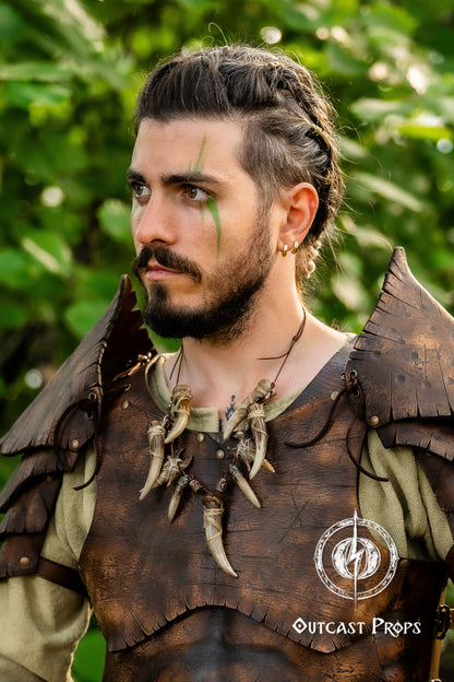 Person wearing a detailed leather outfit with decorative elements, standing outdoors. Celtic Tusk Necklace Viking ornament Tribal Shaman Druid with realistic resin fangs Orc LARP cosplay and post-apocalypse marauder