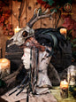 A Celtic adorned tiara with a resin skull, deer horns, feathers, bone pieces, beads, and fangs displayed on a table with a wooden background and candles. Beltane Headpiece tribal deer horns skull and feathers tiara leather and resin