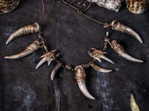 A necklace featuring multiple bone tusk pendants, with a brown and beige color scheme, likely meant as a costume accessory. Celtic Tusk Necklace Viking ornament Tribal Shaman Druid with realistic resin fangs Orc LARP cosplay and post-apocalypse marauder