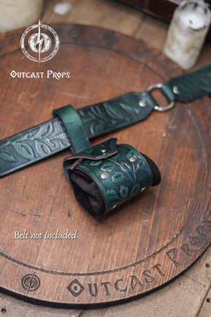 A detailed view of a green floral leather coin pouch attached to a matching embossed belt, shown against a wooden background. The coin bag combines botanical embossing, metal rivets and suede sides, creating an elegant accessory for elven characters, witches, druids or herbalists. Perfect for renfaire and renaissance faire outfits, it holds coins, dice or keys securely as a small fantasy pouch for LARP and immersive costume wear.