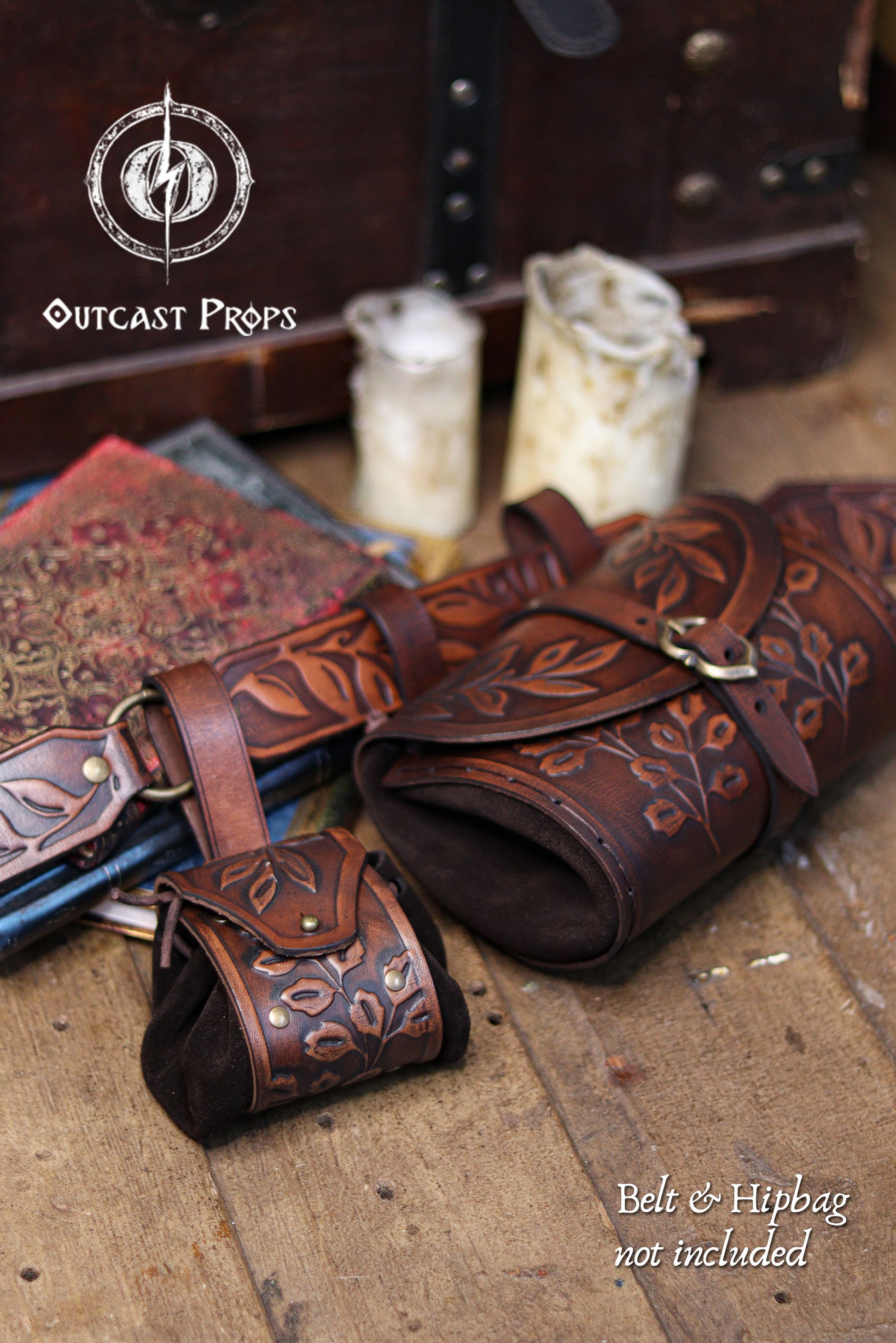 A brown floral embossed leather coin pouch sits beside a large matching hip bag and belt, displayed on wooden floorboards with candles and ornate books in the background. Text Belt and hipbag not included is shown. The pouch’s suede body and botanical carving make it ideal for elves, witches, herbalists and renfaire nobles. Perfect as a leather coin bag or fantasy dice pouch for renaissance faire outfits, LARP or immersive cosplay.