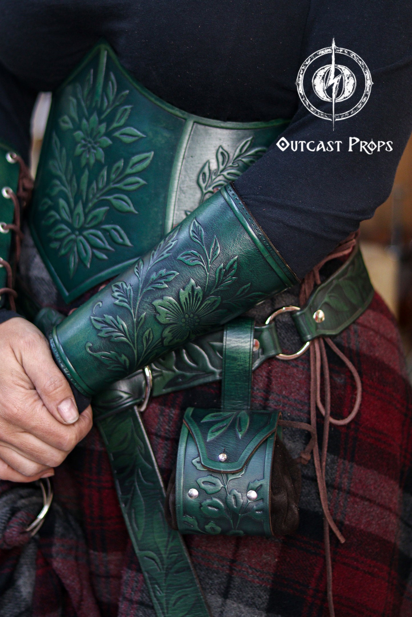 Floral embossed leather bracer and matching green leather coin pouch worn with a renaissance style belt, ideal for elves, witches, herbalists and nobles at LARP or Renaissance Faire events. The vegetable tanned leather shows detailed leaf and wildflower patterns, paired with a soft suede pouch for coins or small items. The image highlights the elegant elven aesthetic and how the pouch hangs securely from the belt loop.