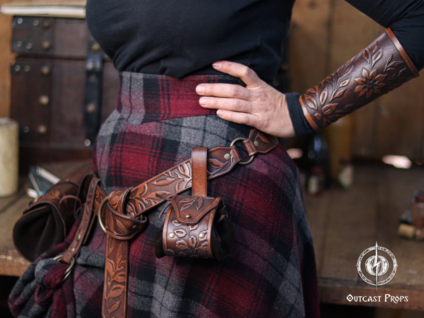 Brown floral leather coin pouch shown in hand as part of a Renaissance Faire herbalist or witch costume, made from vegetable tanned leather and suede. The embossed leaf pattern matches the bracers and belt, ideal for elven characters or nobles who need a stylish pouch for LARP or renfaire. The image shows how the pouch opens with the internal suede bag expanding for coins or trinkets, keeping the elegant fantasy aesthetic intact.