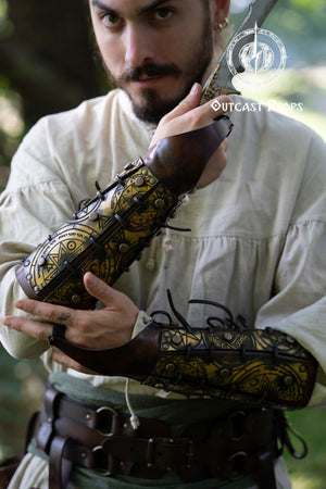 Close-up of a warrior holding a blade while wearing golden magic bracers engraved with alchemist and summoning sigils. The leather has a warm aged finish, laced with black cords and metal studs. Ideal for LARP, cosplay, or fantasy characters like demon hunters or arcane warriors. These ornate leather bracers add a mystical touch to any medieval or fantasy outfit, combining protection, storytelling, and artisanal detail. Demon Hunter Leather Bracers Armor for LARP Cosplay Witch Warlock Alchemist Magic Rune