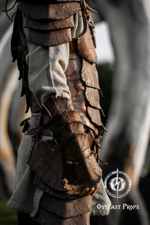 Detail of the hand-crafted Dragon Scales leather armor by Outcast Props. Features layered brown scales on shoulder, chest and forearm, with visible rivets and medieval textures. Artisan leather work, vegetable-tanned and weathered for LARP, fantasy cosplay or themed photoshoots. A warrior costume for Ren Faire or fantasy characters like hunters, druids, or rangers.