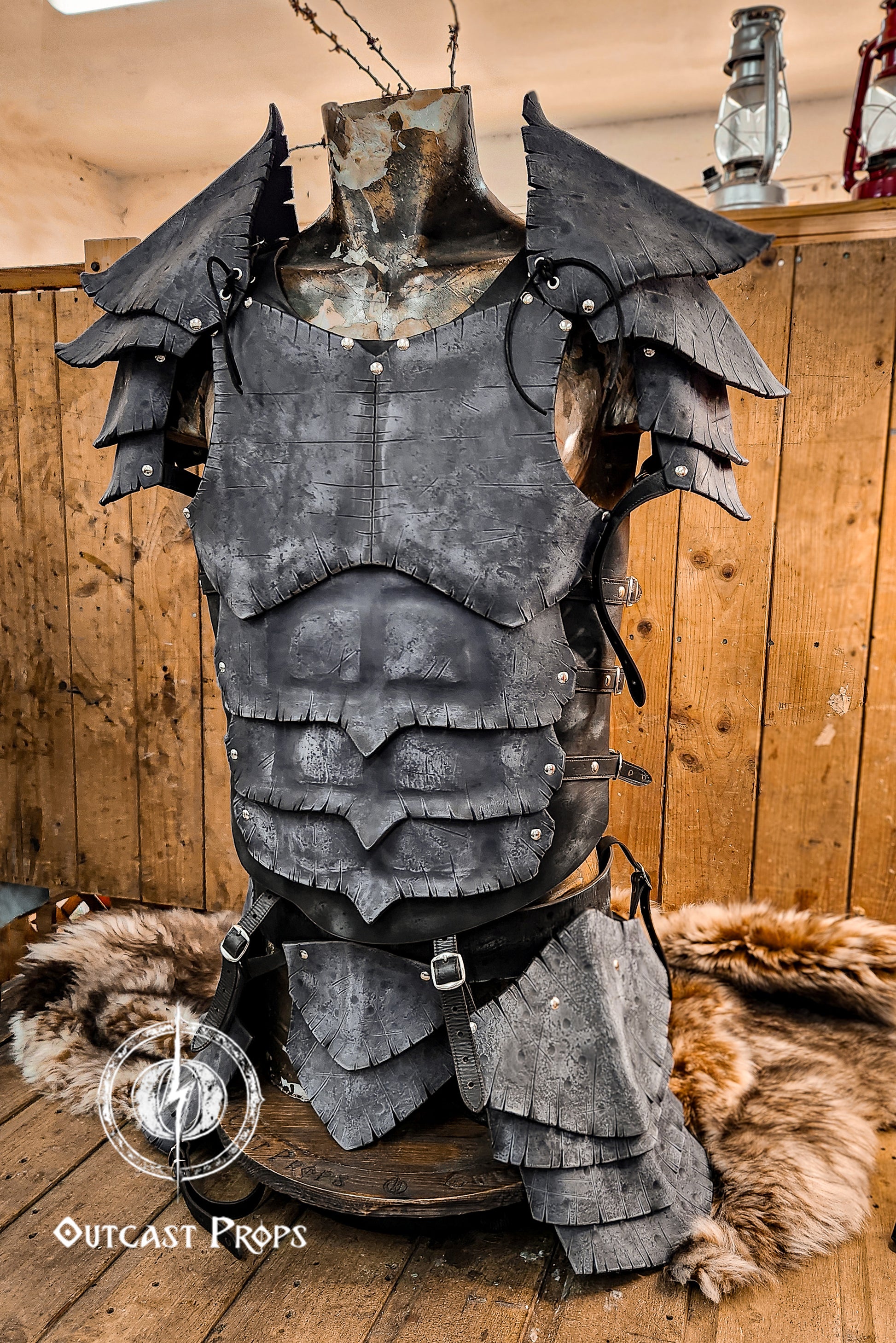 Side view of black leather dragon scale armor set shown on a rustic mannequin. The set includes sculpted abdominal plates, detailed shoulder guards, and reinforced straps. Designed for dark fantasy LARP, villain cosplay, or medieval mercenaries. Ideal for portraying powerful warriors or cursed knights. The realistic finish and structured silhouette evoke a sense of strength and mystery. Made with premium leather using Outcast Props' artisanal methods.Medieval armor on a wooden stand with Outcast Props logo.