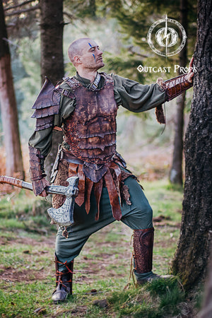 Full body shot of a LARP warrior in brown dragon scale armor, standing in the forest holding a fantasy axe. The leather bracer features rugged scale patterns and is perfect for orc characters, monster slayers or forest rangers. Handmade from high-quality vegetable-tanned leather and uniquely aged by hand. This cosplay bracer is built for epic campaigns and immersive roleplay.