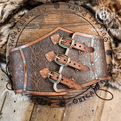 Leather underbust with embossed design and gold buckles on a wooden background. Leather Corset. Elegant underbust por cosplay and larp. 