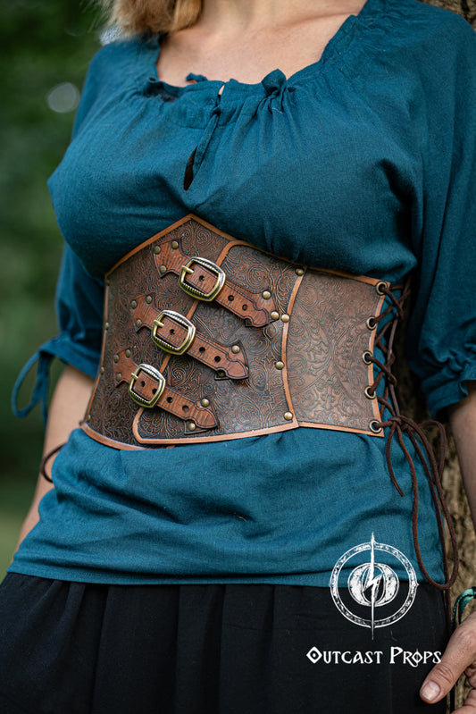 Person wearing a blue top with a leather corset belt featuring metal buckles. Embroidered Leather Underbust Corset – Elegant Brown Waist Cincher for Noble LARP Outfits, Steampunk and Fantasy Glamour
